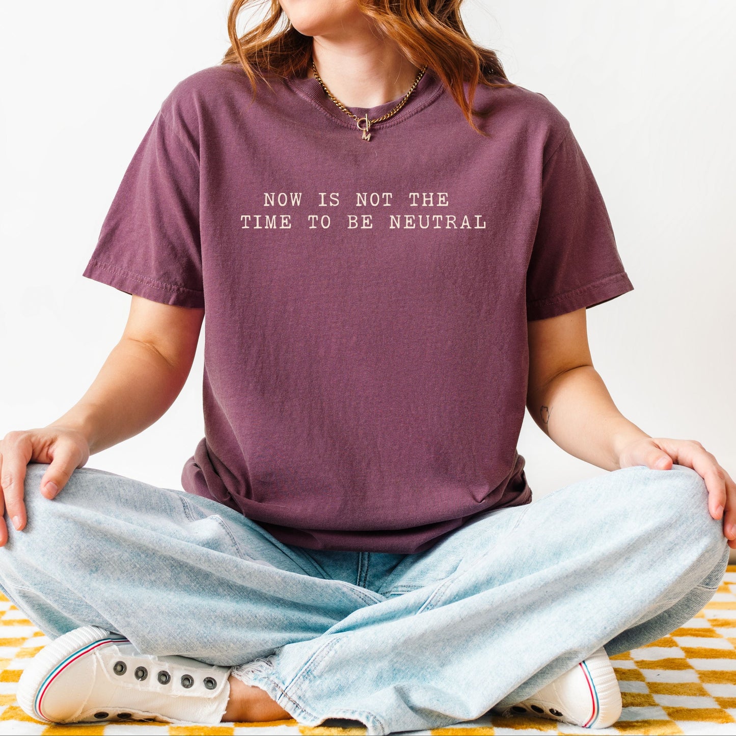 Person sitting cross-legged wearing a purple t-shirt with text, on a yellow and white checkered floor.