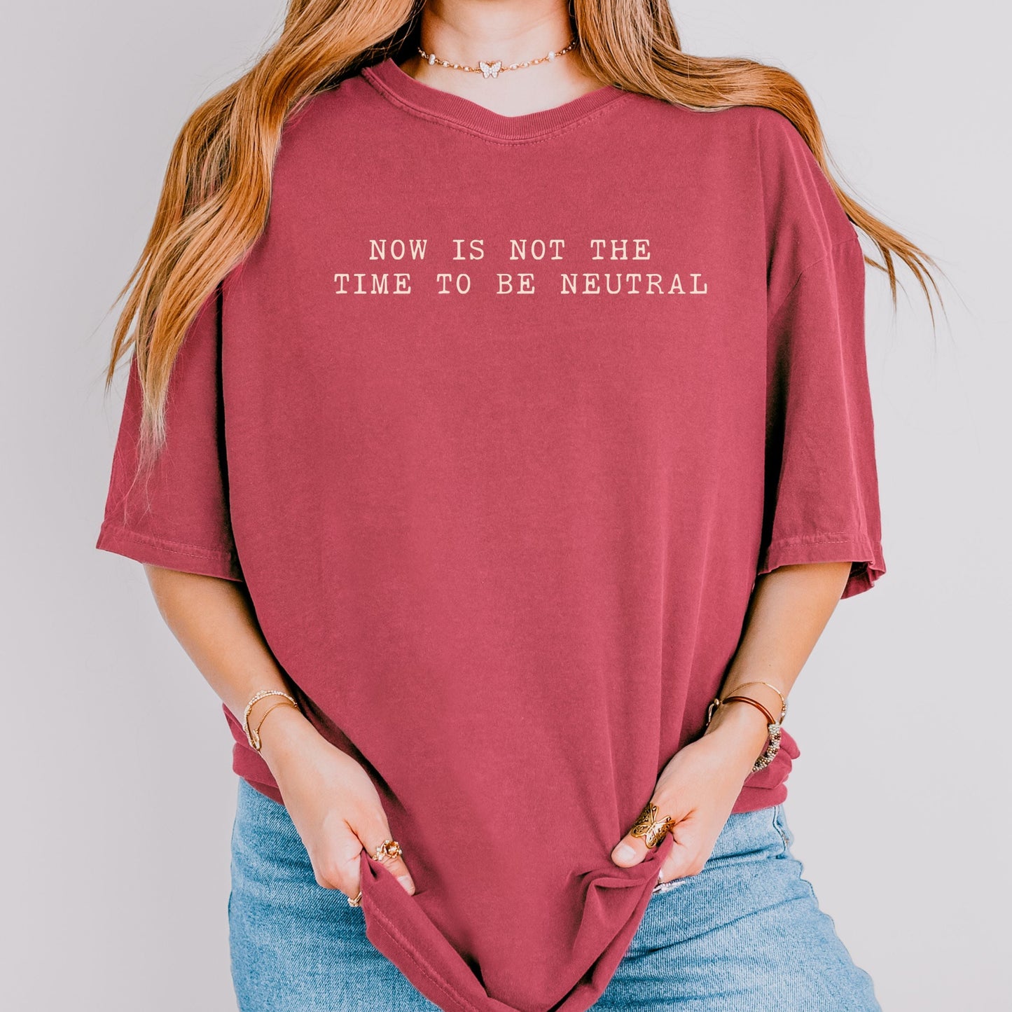 Person wearing a maroon t-shirt with a quote and logo on a plain background